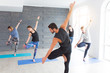 © uv_group - Yoga men instructor teaches group of people, fitness, sport and healthy lifestyle concept. Young women with personal trainer doing yoga exercises on mat in gym studio
