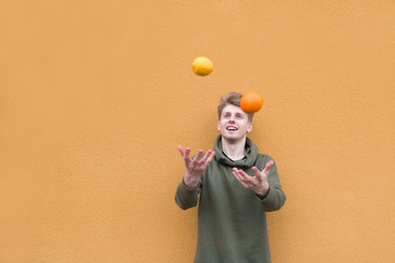 Happy young man juggles with orange and lemon against the background of an orange wall.