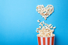 I Like Watching Films. Spilled Popcorn In The Shape Of Heart And Paper Bucket In A Red Strip On Blue Background. Copy Space For Text