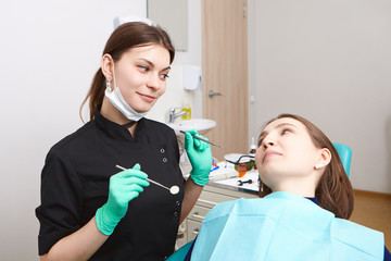 People, healthcare, dentistry, job and occupation concept. Candid shot of experienced attractive young brunette woman dentist holding dental tools while checking teeth of female patient for cavities