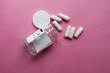 white pills from a jar on a pink background