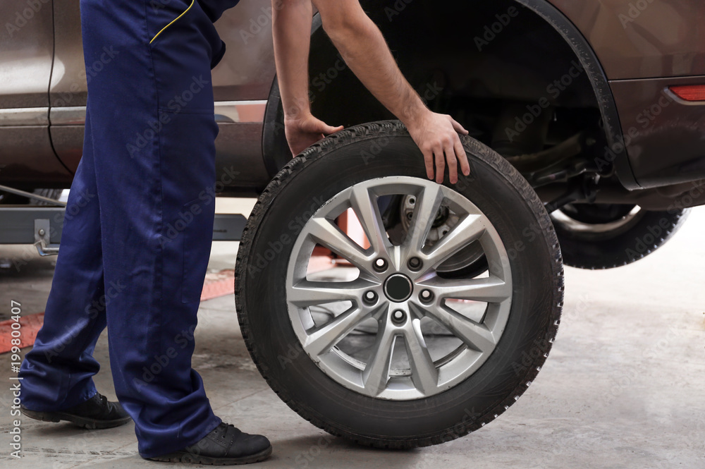 Mechanic with car wheel in repair shop. Tire service - obrazy, fototapety, plakaty 