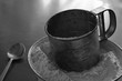 Old stainless steel cup flour sifter lies in a white enamel bowl on an old scratched table