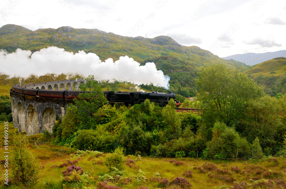 An old train on a mountain valley. Steam comes from the pipe. Scotland. - obrazy, fototapety, plakaty 