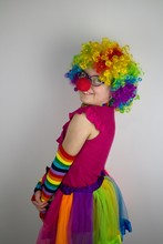Little Girl With Glasses And Red Nose In Colorful Clown Costume.
