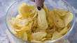 Two female fingers take snack from bowl of crispy potato chips