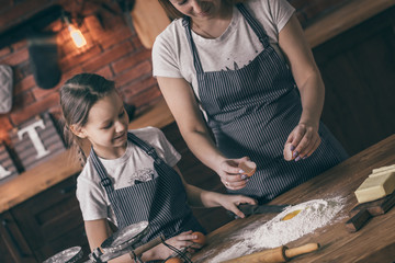 Poster - Crop mother and little girl putting egg to flour while cooking dough.