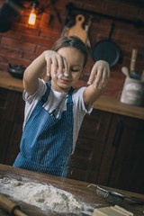 Poster - Little girl standing at kitchen table and cooking with flour at home.