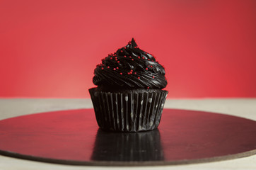 Black cupcake with sprinkles on red background 