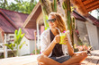 Beautiful young woman sits in a cafe in the tropics and drinks a cocktail of tropical fruits