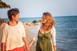 A beautiful mature woman with her adult daughter is walking along a tropical beach, relaxing together. Mothers Day