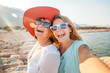 © olezzo - An attractive middle-aged woman with her adult daughter doing selfie on the beach, vacation and travel, cruise and sea