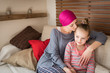 © andreaobzerova - Young adult female cancer patient spending time with her daughter at home, relaxing on the couch. Cancer and family support concept.