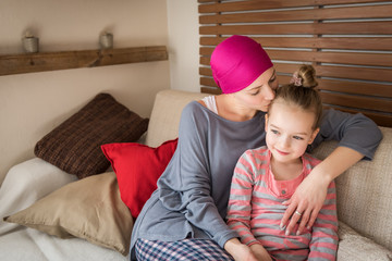 Young adult female cancer patient spending time with her daughter at home, relaxing on the couch. Cancer and family support concept.