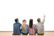 The four people sit on the floor and gesture on a white wall background