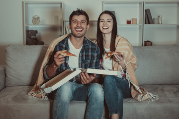 The happy couple eating a pizza and watch a movie on the sofa