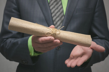 Businessman holds in hand a rolled up document scroll. Signing of an agreement. Conclusion of a business contract. Business deal concept. Special offer..