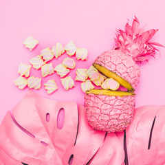 Wall Mural - two painted in pink color halfs of the pineapple with tropical palm leaves of monstera and marshmallow. fashion pink concept. minimal and surreal. summer food.