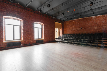 Loft style. Hall with black chairs for webinars and conferences. A huge room with large Windows, surrounded by brickwork, and parquet floors. For film and theatre productions