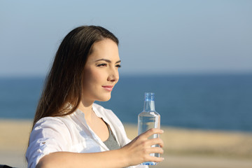 Wall Mural - Serious woman holding a water bottle on the beach