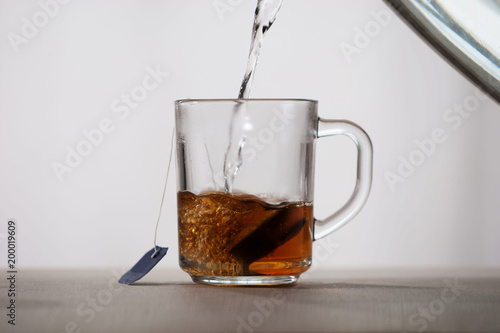 Fotografie, Obraz Boiling water is poured into a glass mug with a tea bag