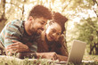 © Mladen - Young African American couple lying down in park and using laptop.