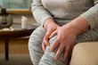 © Suzi Media  - Senior woman suffering from pain in knees at home. Holding her knee and massaging with hands, feeling exhausted, sitting on sofa in living room. Close-up. Medications and pills on table