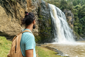 young bearded man looking at waterfall, hunua falls, new zealand