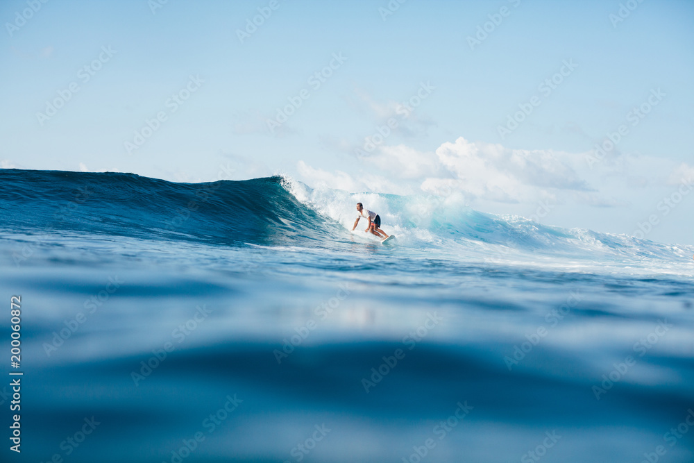 handsome athletic man surfing on blue wave - obrazy, fototapety, plakaty 