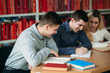 © Aleksandr - University students sitting together at table with books and laptop. Happy young people doing group study in library
