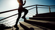 sporty female jogger running upstairs on seaside during sunrise