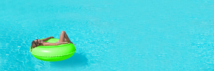 Young woman on giant inflatable swimming ring relaxing in swimming pool, panoramic summer and vacations concept