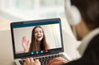 © fizkes - Young girl waving from laptop screen at man in headphones. Happy teen greeting her boyfriend, friends exchange and learn foreign languages, couple communicating via video call app. View over shoulder.