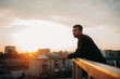 © Stanislav - Young man is pondering on terrace of roof against background of cityscape at sunset.