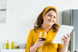 © LIGHTFIELD STUDIOS - smiling beautiful woman holding glass of red wine and using tablet in kitchen