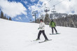 © Brocreative - A young skier and a snowboarder skiing and boarding down a ski slope with the chair lift in the background. A fun winter day at the ski resort