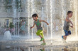Happy kids have fun playing in city water fountain on hot summer day.
