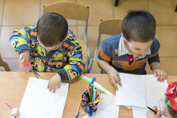 Two little boys are sitting at the desk and write