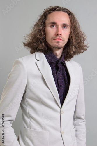 Guy With Long Curly Hair Businessman In A White Jacket On A Gray