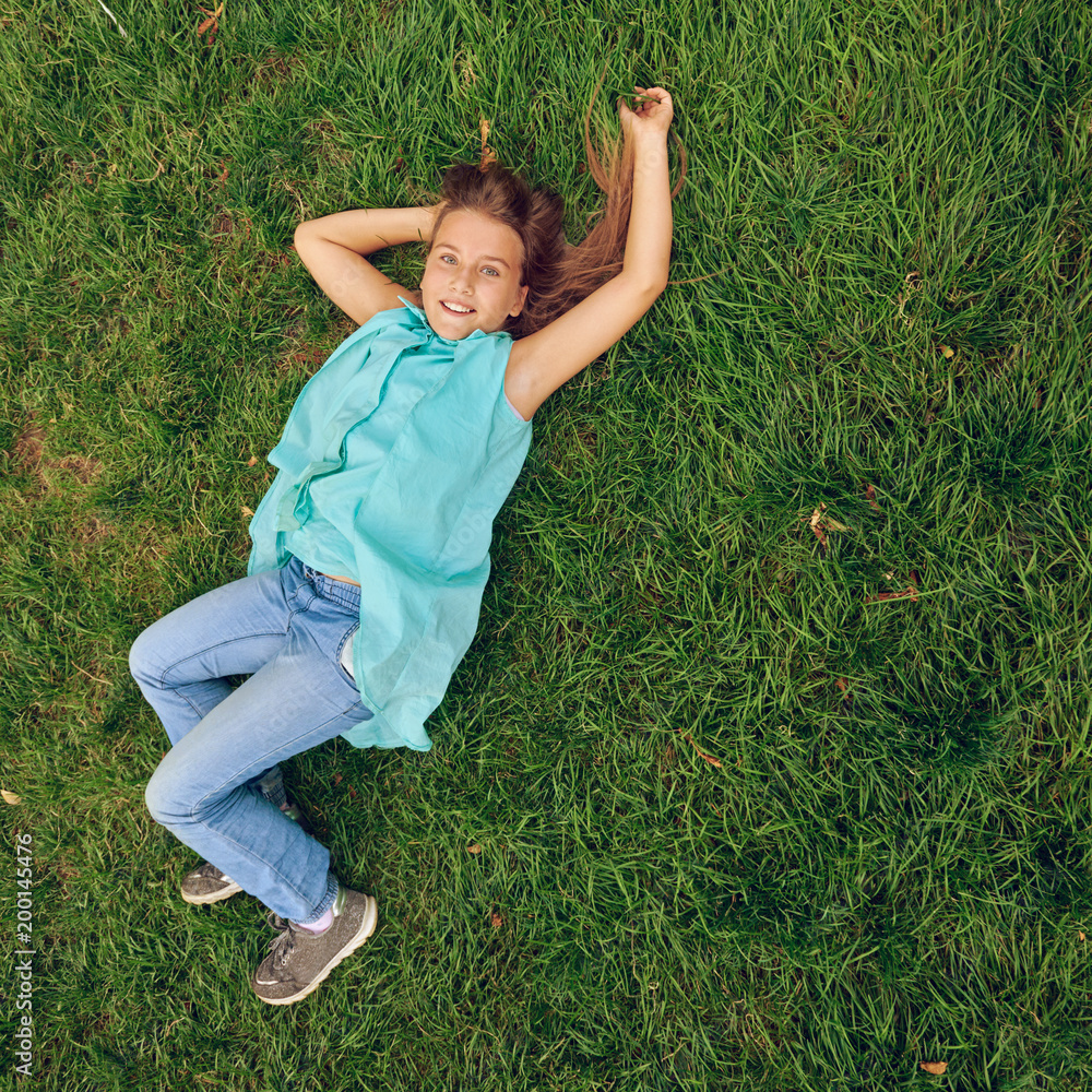 Portrait of smiling little girl lying on green grass, image with toning ...