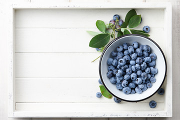 Wall Mural - Fresh ripe blueberries with leaves in bowl in white wooden tray