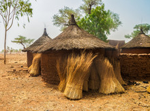 Traditional Huts In An African Village Of Burkina Faso With Some Bundles Of Straw Stored Against Their Circular Walls Made Of Mud Bricks.