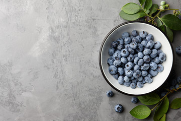 Wall Mural - Fresh ripe blueberries with leaves in bowl on gray stone background, top view