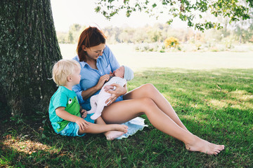 Mother with newborn baby and older child on nature.