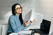 © mnelen.com - tired young girl freelancer in blue shirt and glasses working on laptop, holding documents