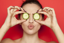 Sexy Young Woman Posing With Slices Of Cucumber On Her Face On Red Background