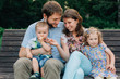 © beatleoff - young laughing family of four sitting on wooden bench. Parents with cute kids.