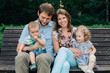 © beatleoff - young laughing family of four sitting on wooden bench. Parents with cute kids.