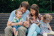 © beatleoff - young laughing family of four sitting on wooden bench. Parents with cute kids.