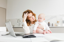 Portrait Of Thoughtful Business Woman Holding Her Little Baby While Sitting At The Table And Working Isolated